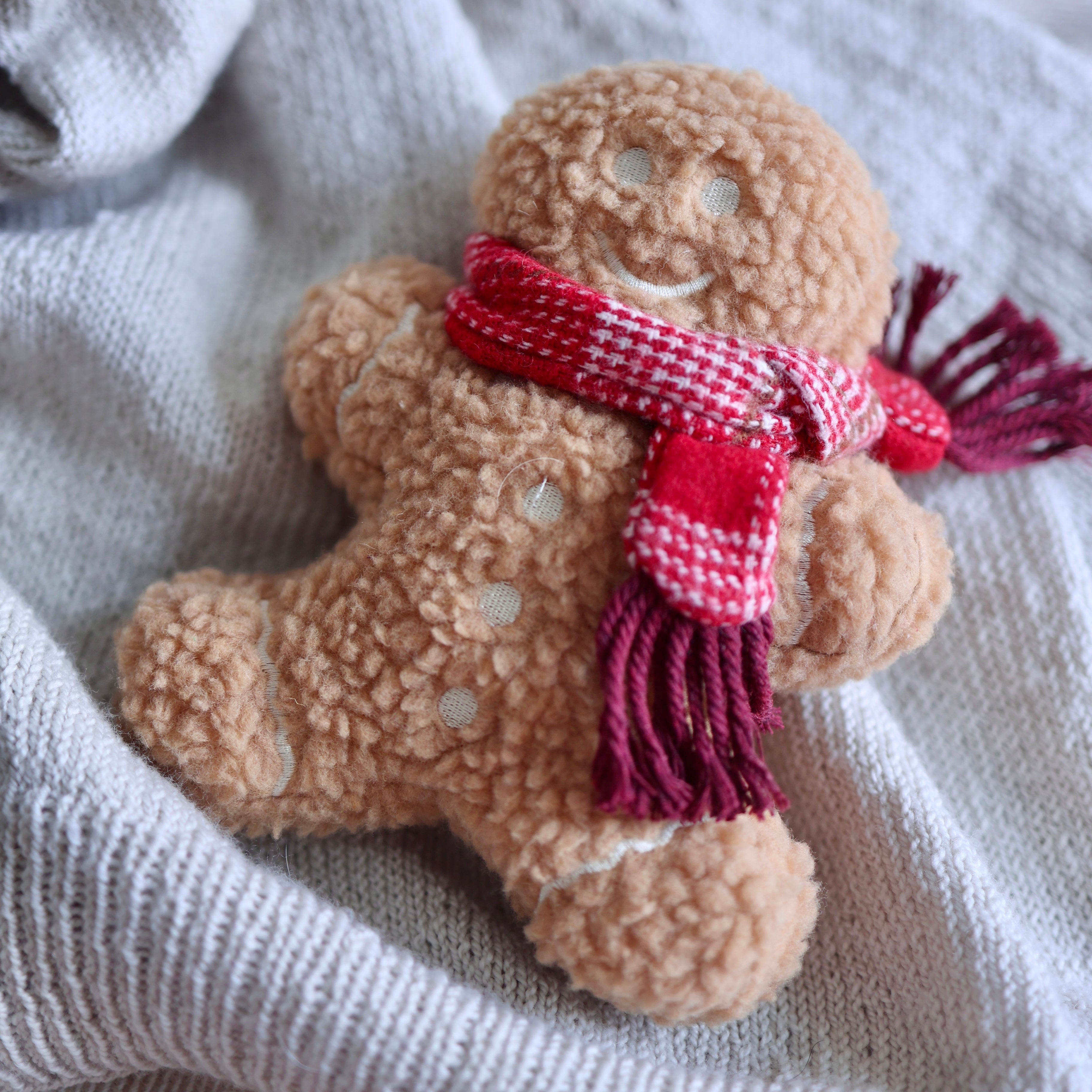 Plush gingerbread man toy with a red scarf on a textured fabric background
