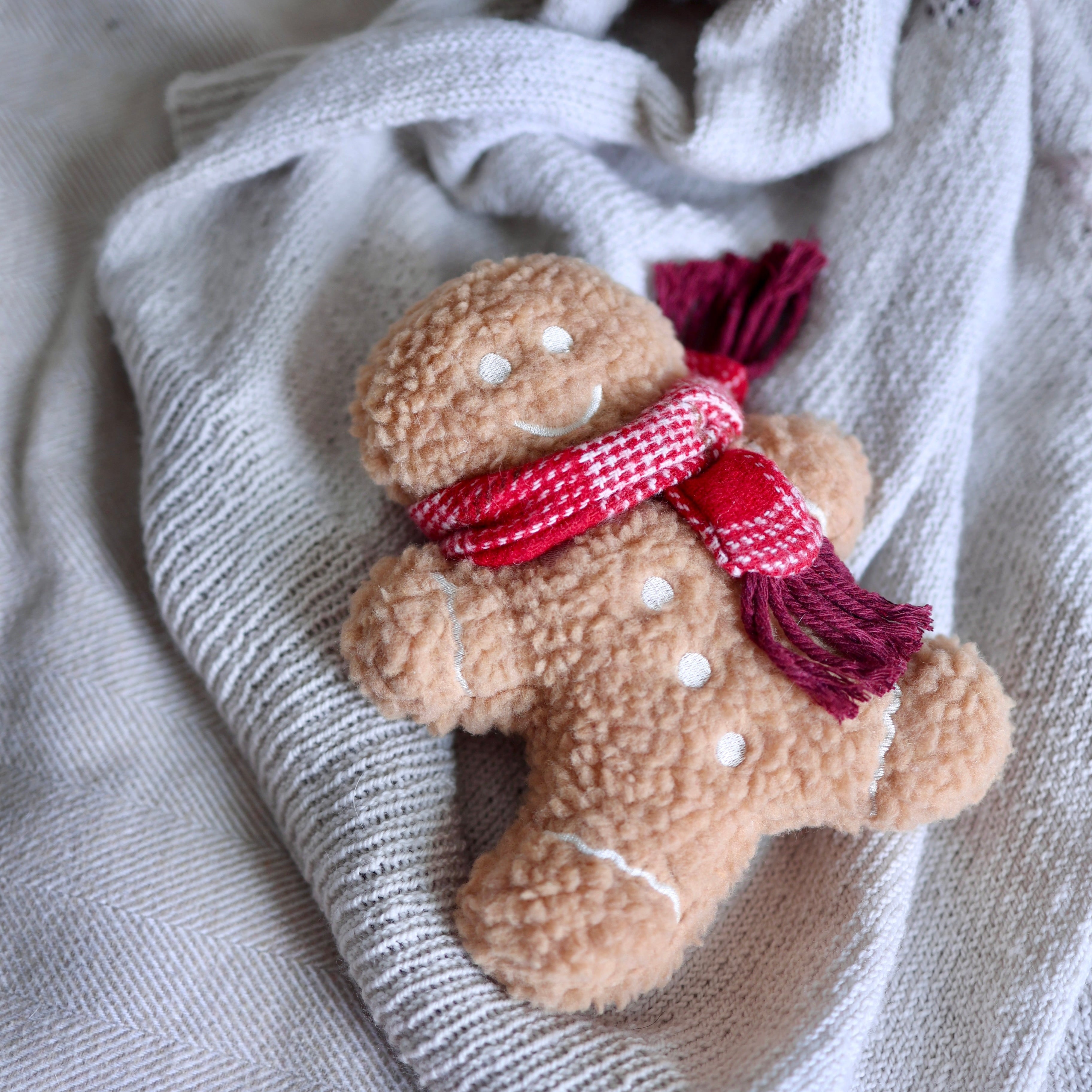 Toy gingerbread man with a red scarf on a textured fabric background