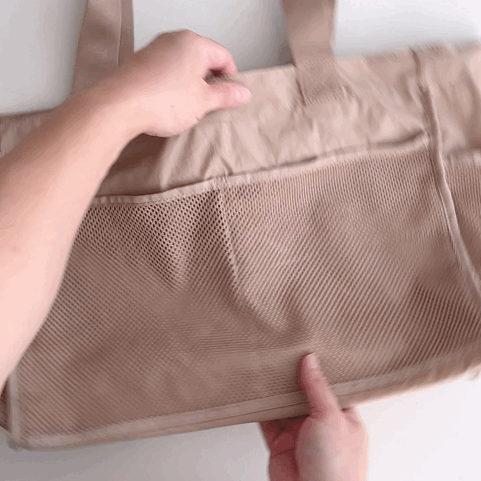 Hands open a spacious mesh pocket on a beige tote bag, highlighting its organizational features.