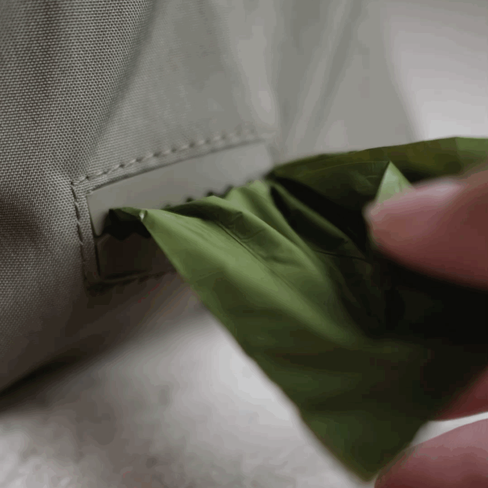 Hand pulls a green dog waste bag from the built-in dispenser of a gray dog walking bag.