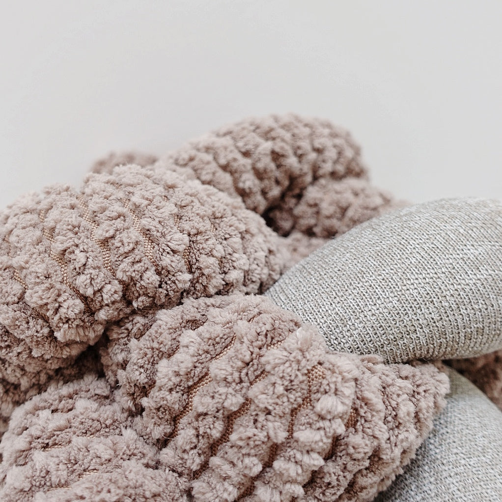 Fluffy brown and gray throw pillows create a cozy pile on a neutral background.