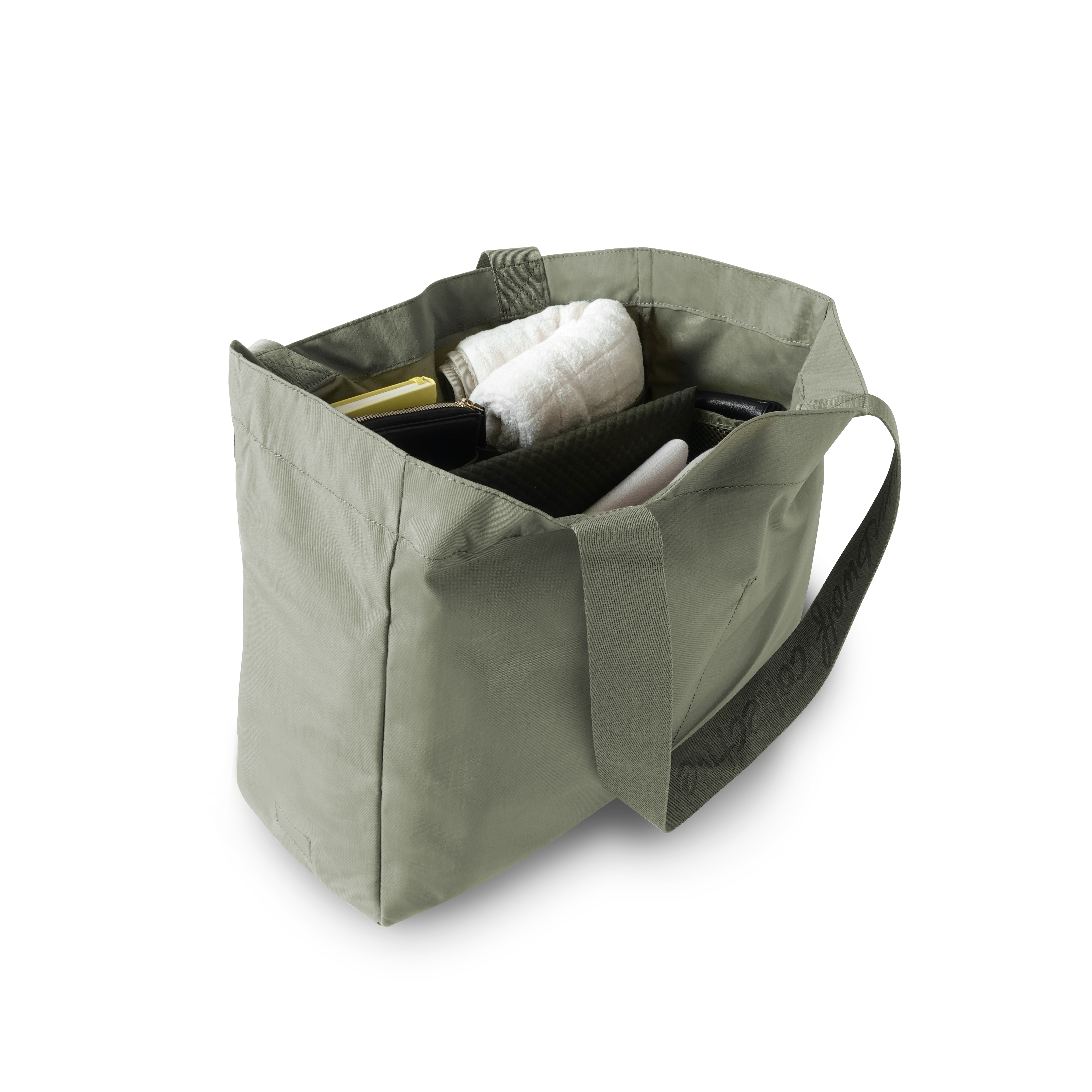 An open sage green tote bag displays organized essentials, including a book, wallet, and water bottle.