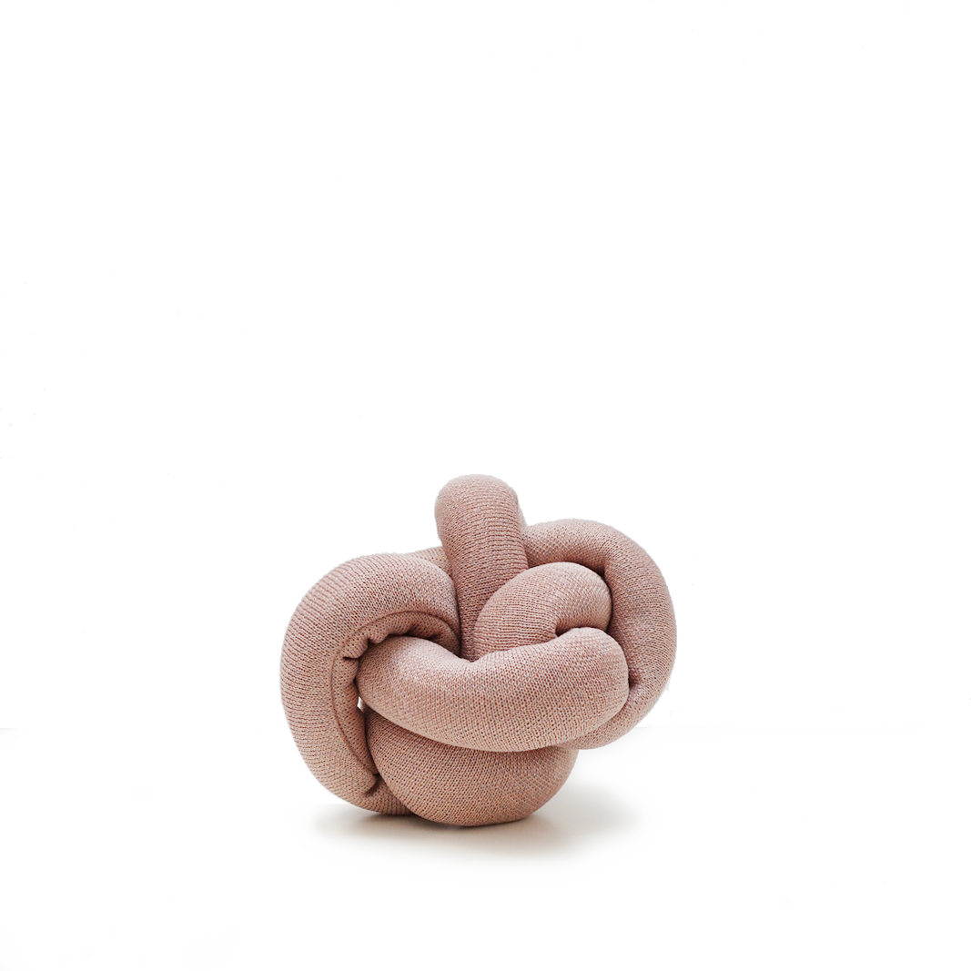 A soft pink knotted cushion rests on a white surface.