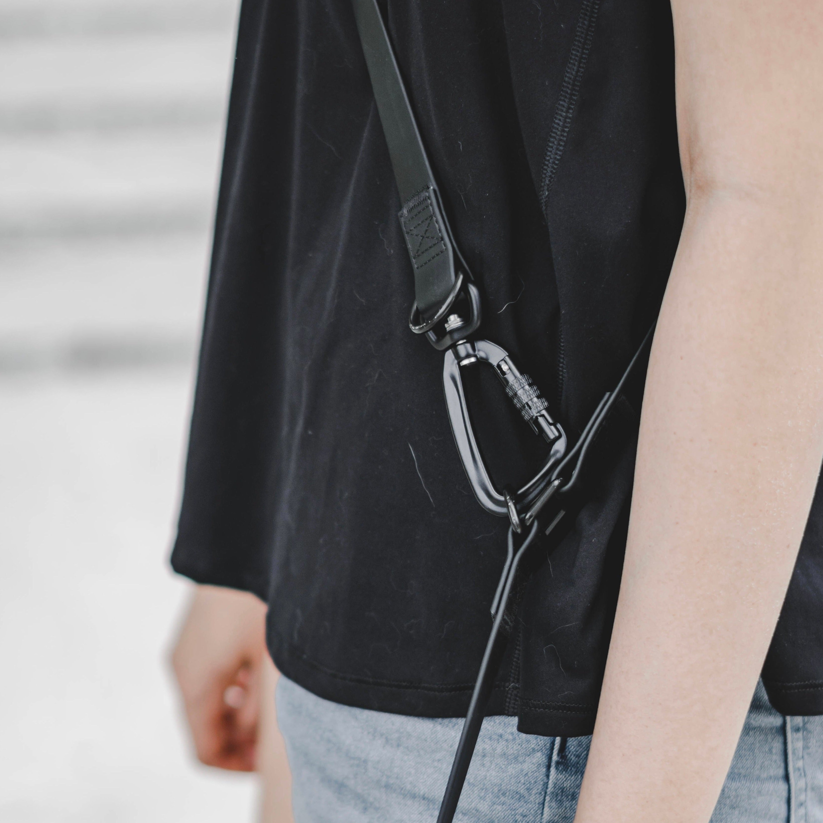Close-up of a black carabiner clip securing a strap to a black shirt. 
