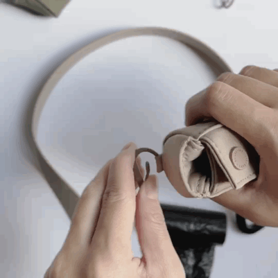 "Hands attach a beige dog poop bag dispenser to a matching leash with a metal clasp." 
