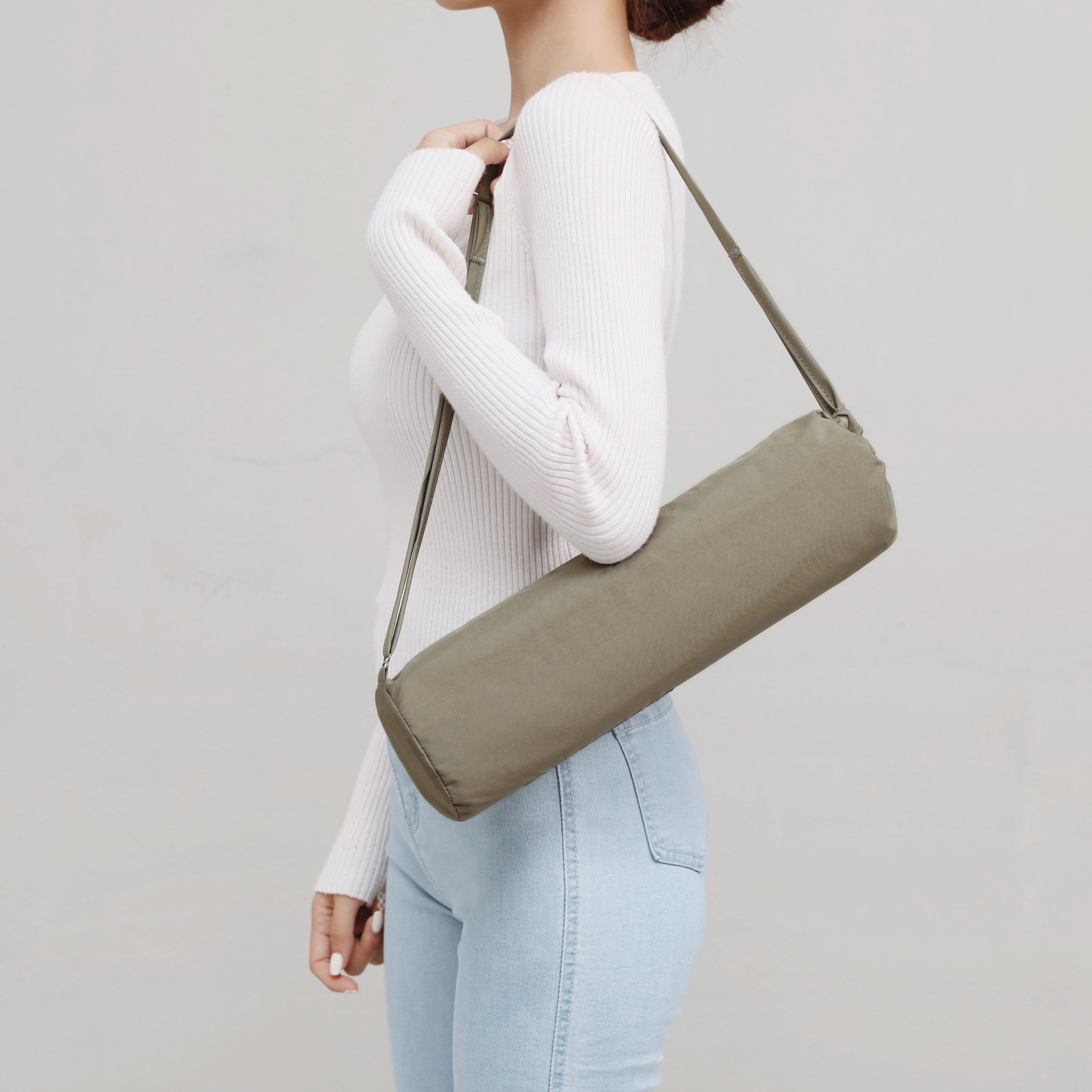 Woman carries olive green yoga mat bag over her shoulder. 
