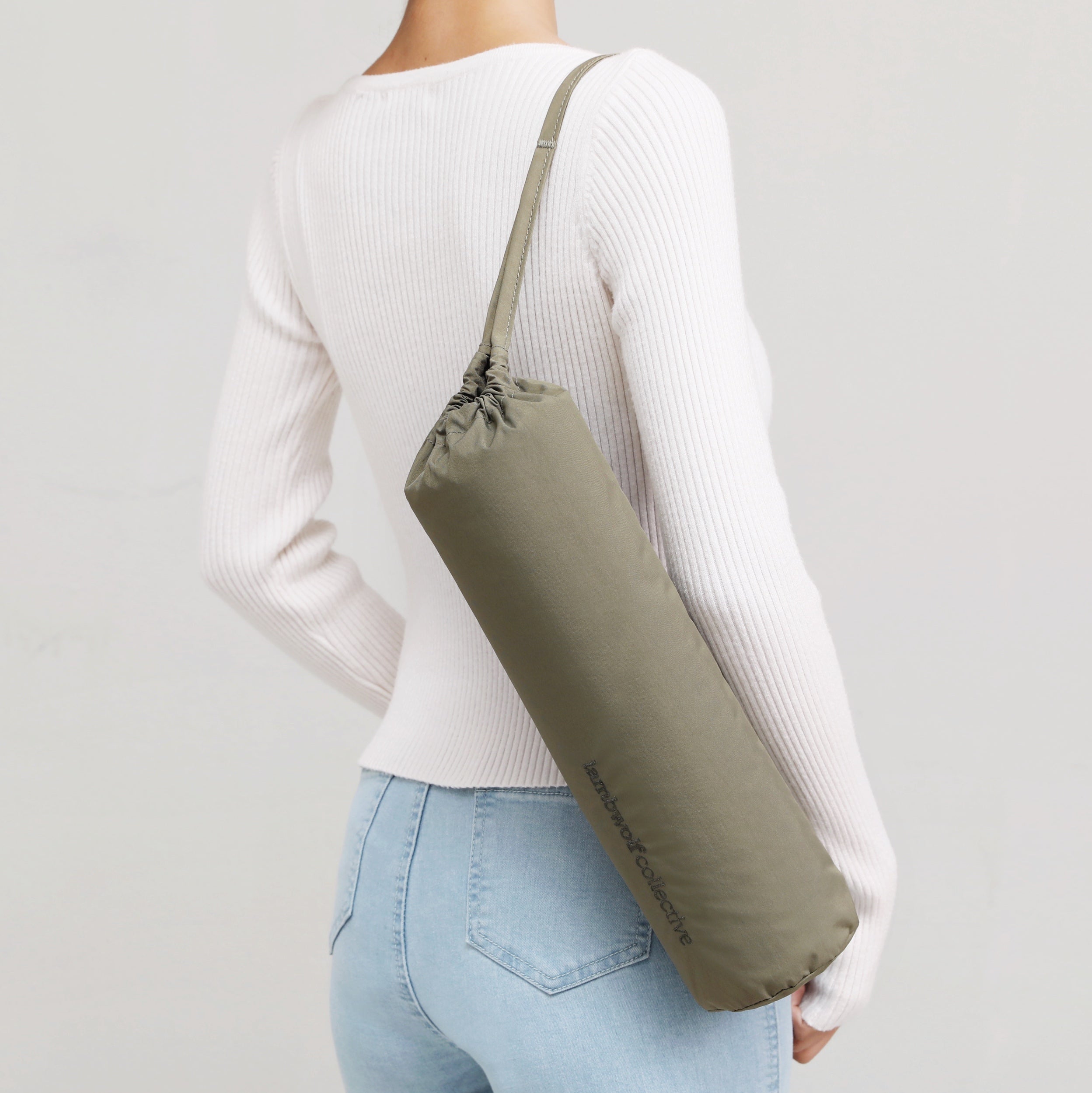 Woman slings a khaki green LamGolf Collective golf bag over her shoulder. 
