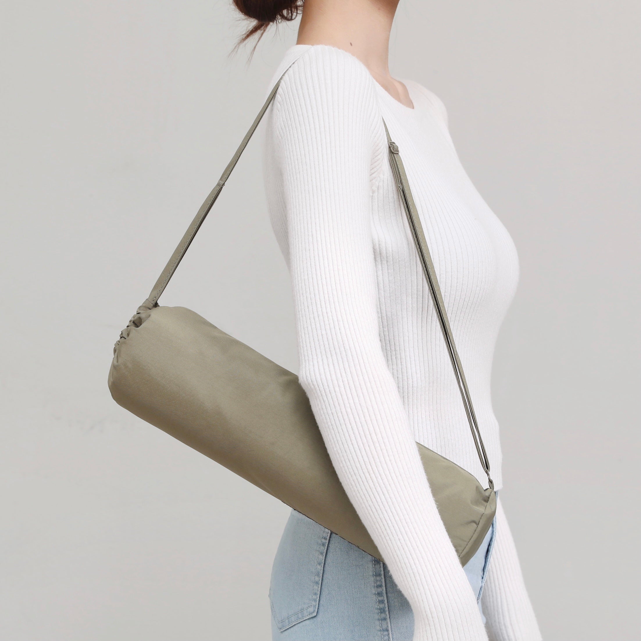 Woman slings a lightweight, olive green yoga mat bag over her shoulder. 

