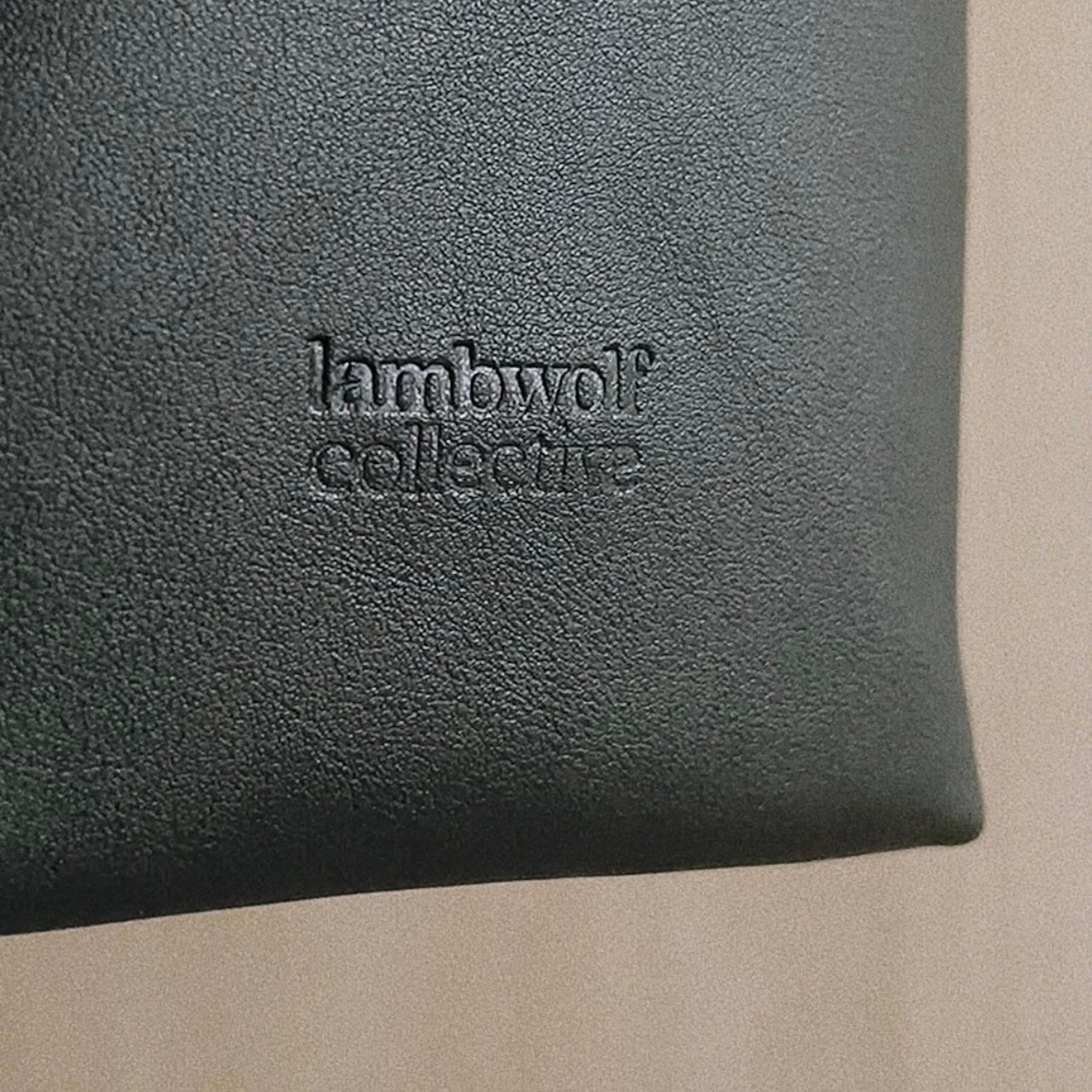 Close-up of the Lambwolf Collective logo embossed on a black leather accessory. 
