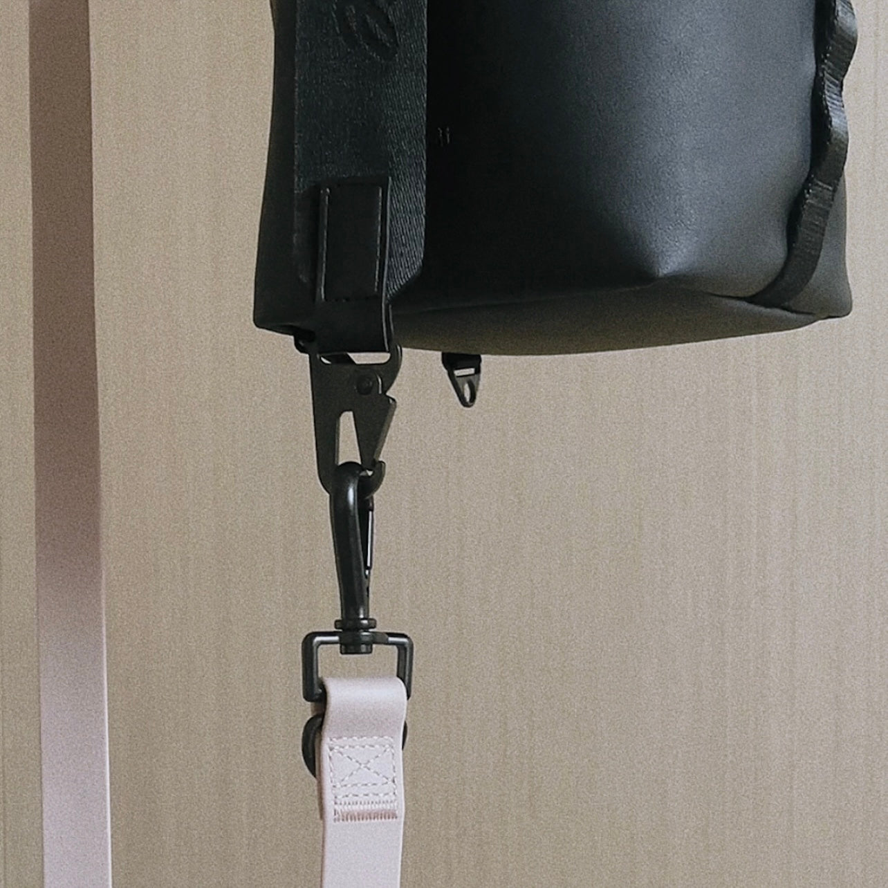 Black leather handbag hangs from a blush-colored adjustable strap with a silver metal clasp. 

