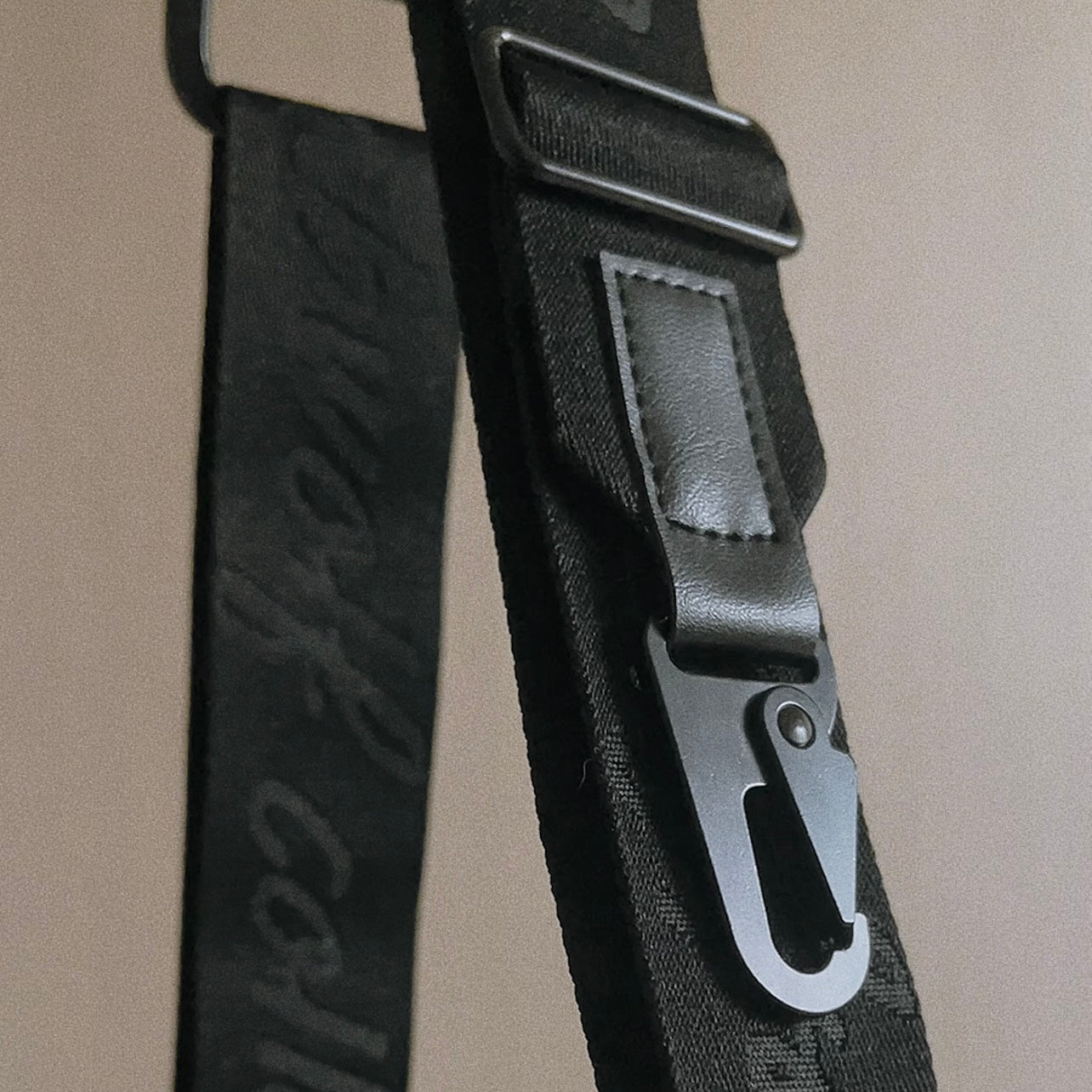 Black nylon bag strap with embossed logo and metal clasp closure. 
