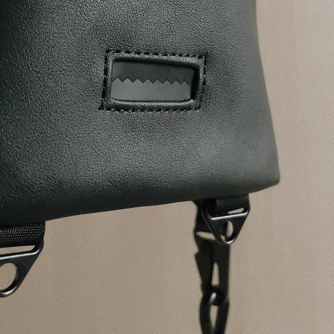 Black leather backpack strap connects to the bag with a rectangular black metal buckle. 
