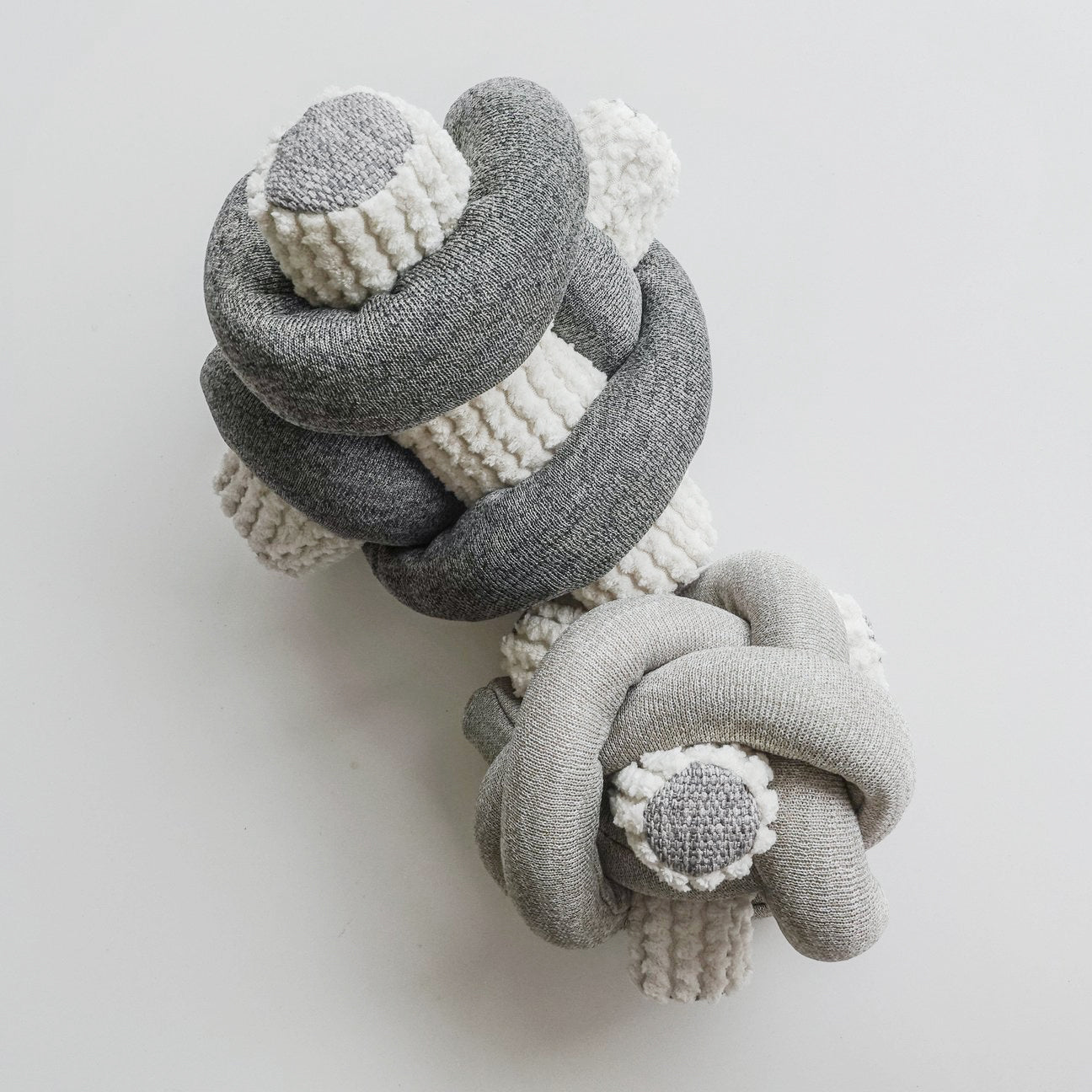 Gray and white knotted fabric art hangs on a white wall. 
