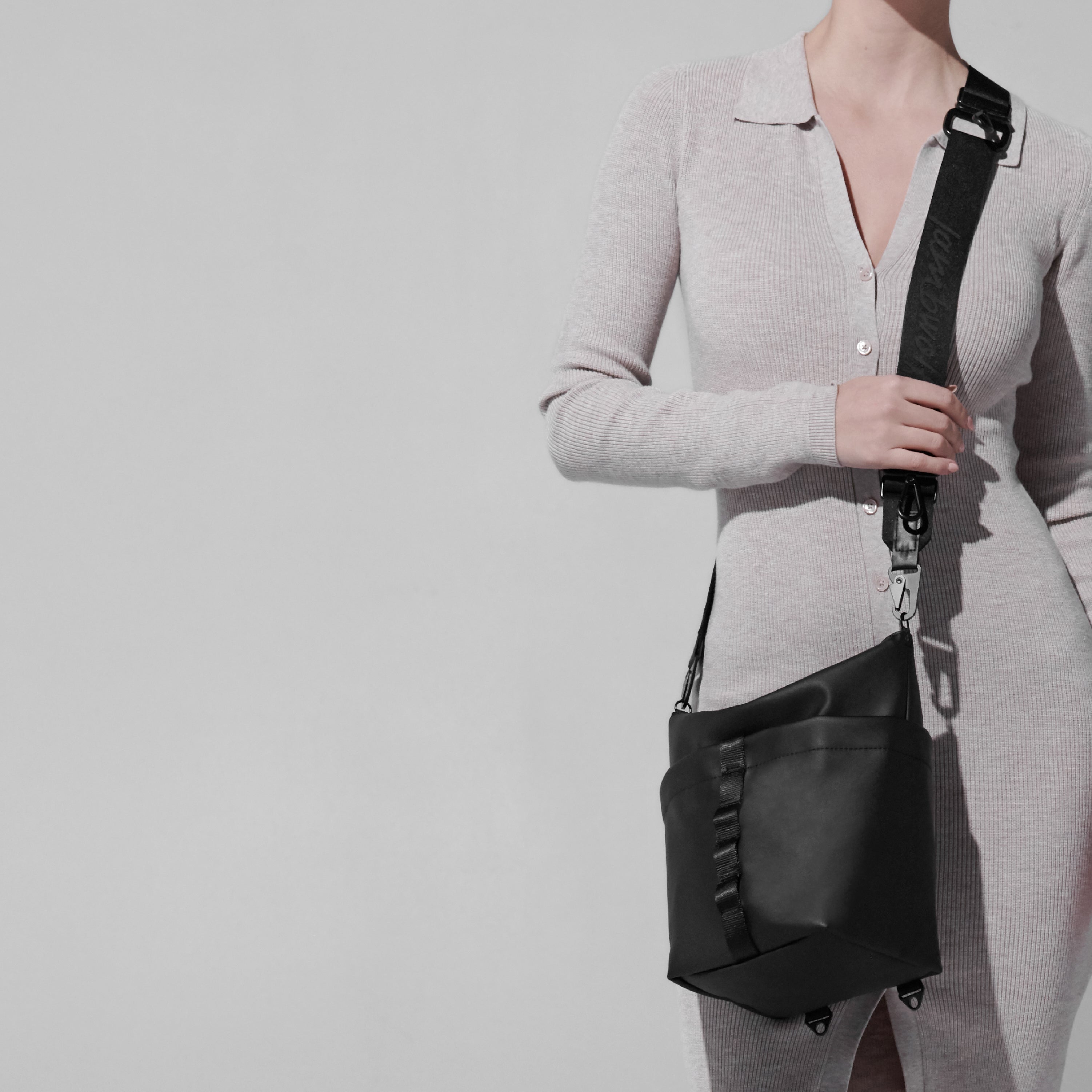 Woman models a black crossbody bag with a wide, adjustable strap. 
